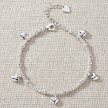 Silver bracelet with heart charms on a linen textured background.