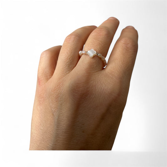 Hand wearing a pearl bead ring with a white clover.