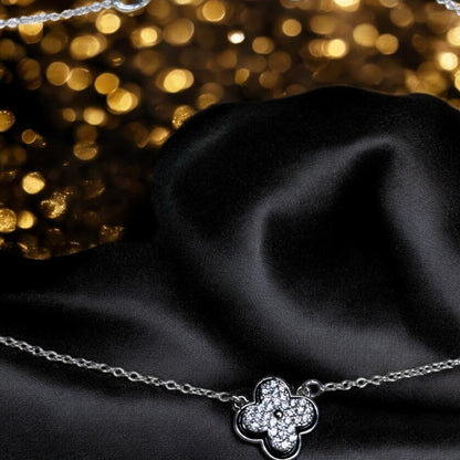 Silver necklace with a clover-shaped pendant on black fabric with gold glitter background.