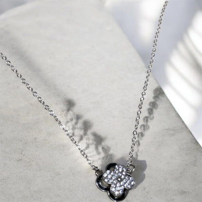 Silver necklace with a spinning clover pendant on a light grey surface.