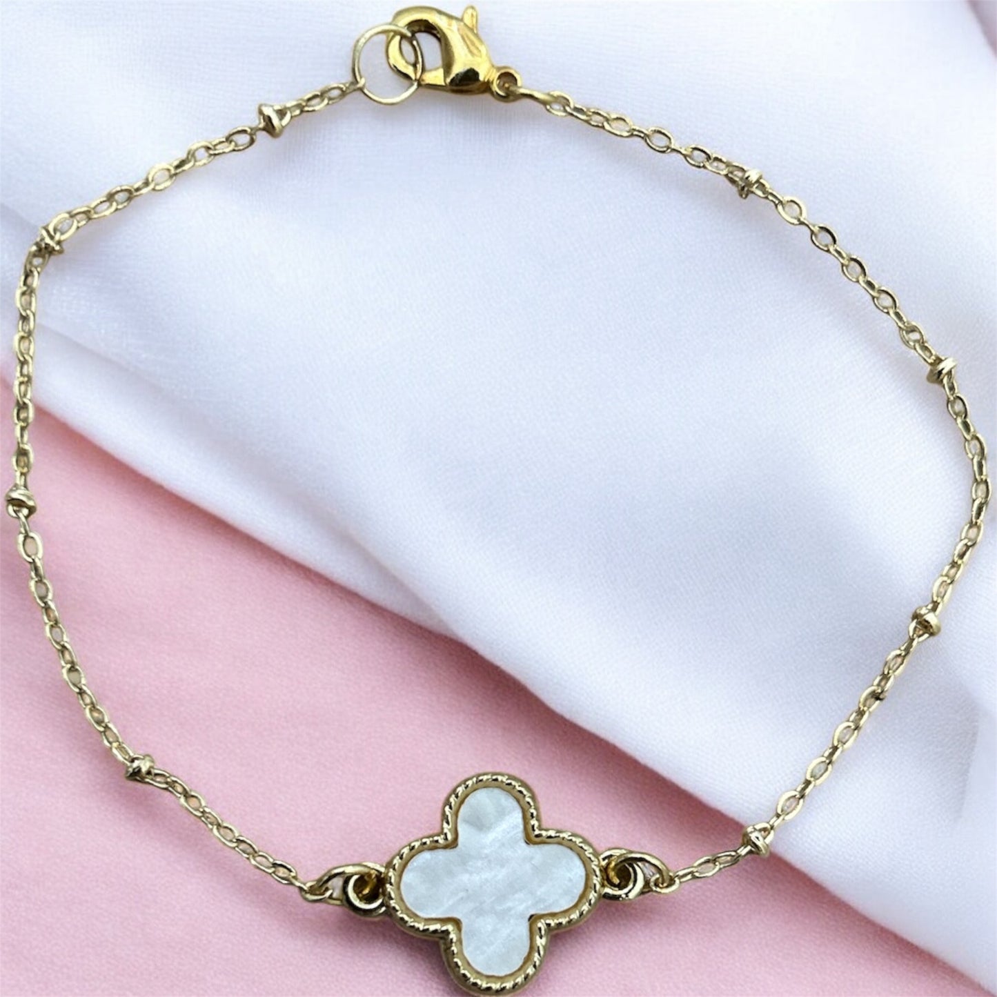 Gold bracelet with a clover-shaped charm on a pink and white background