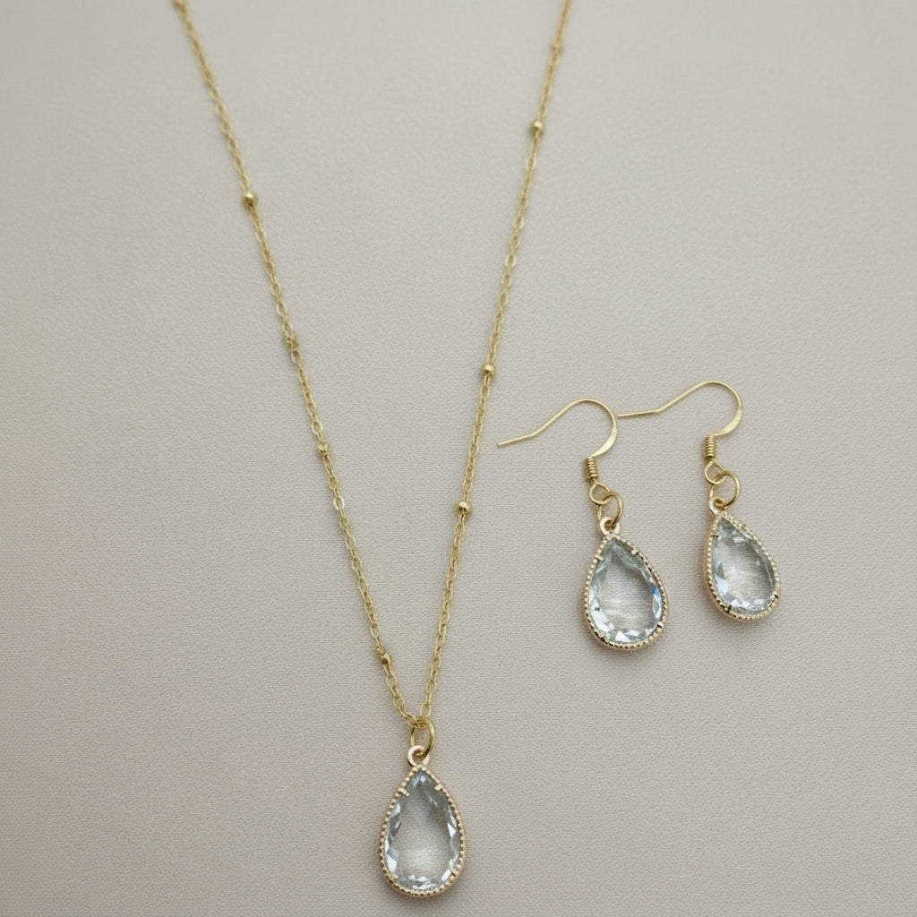Gold necklace and earrings with teardrop-shaped stones on a textured surface