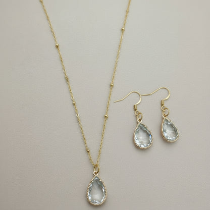 Gold necklace and earrings with teardrop-shaped stones on a textured surface