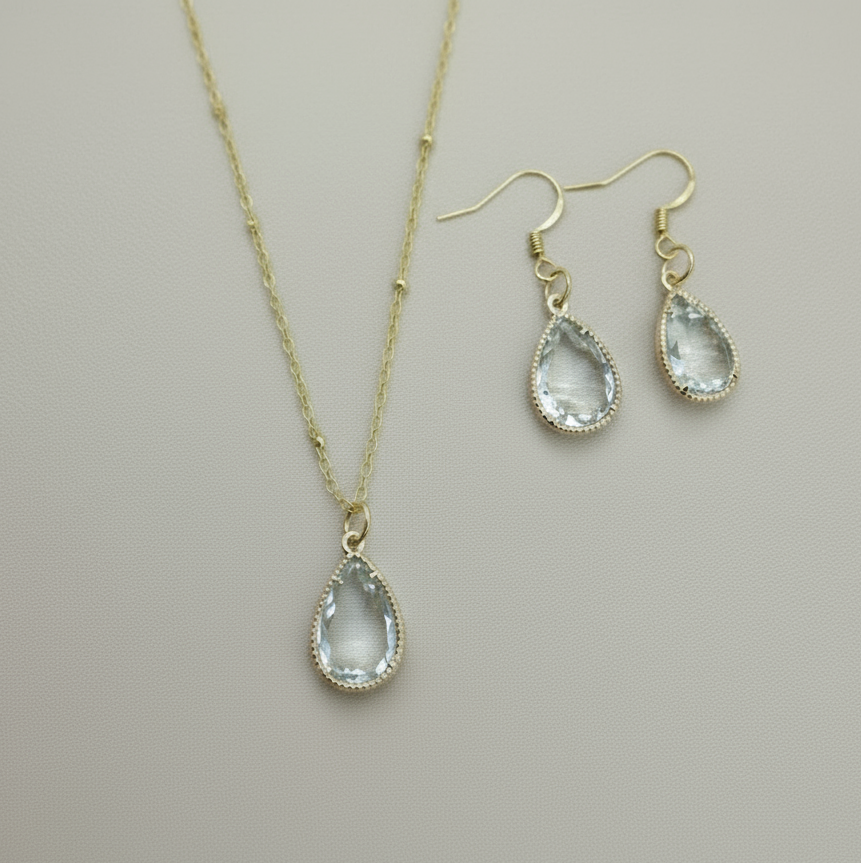 Gold necklace and earrings with clear teardrop stones on a light background