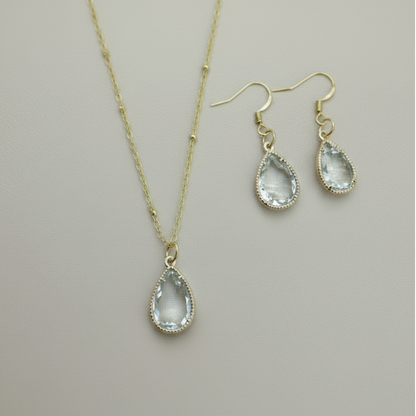 Gold necklace and earrings with clear teardrop stones on a light background