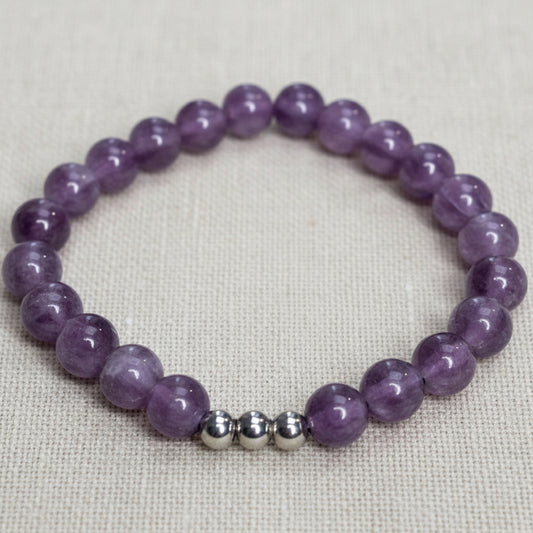 Purple beaded bracelet with silver beads on a plain surface.