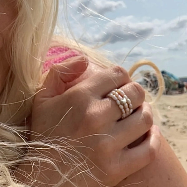 Close-up of a hand with multiple pearl rings on a beach.