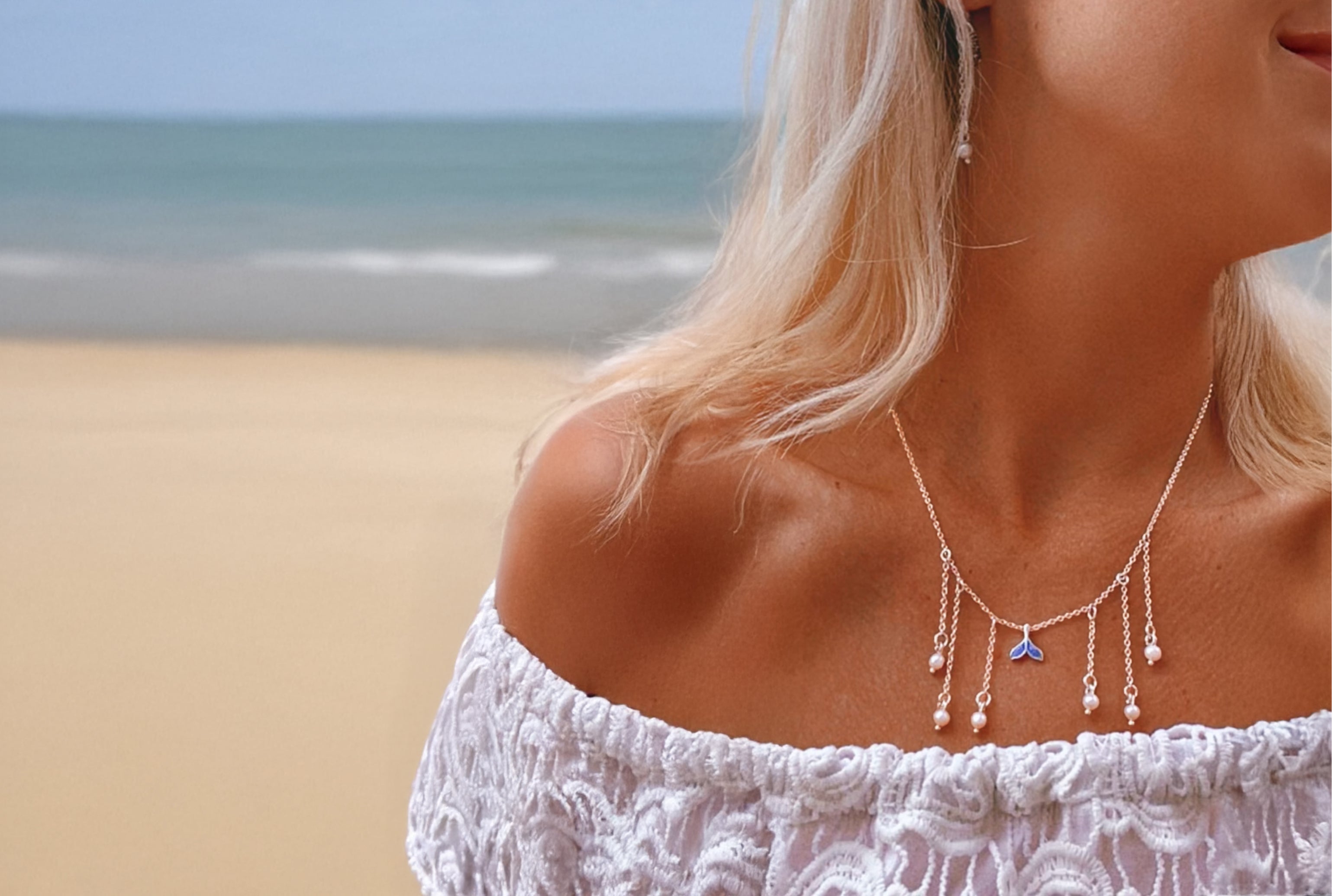 Woman wearing a necklace with a blue mermaid tail pendant and chain drop pearls on a beach