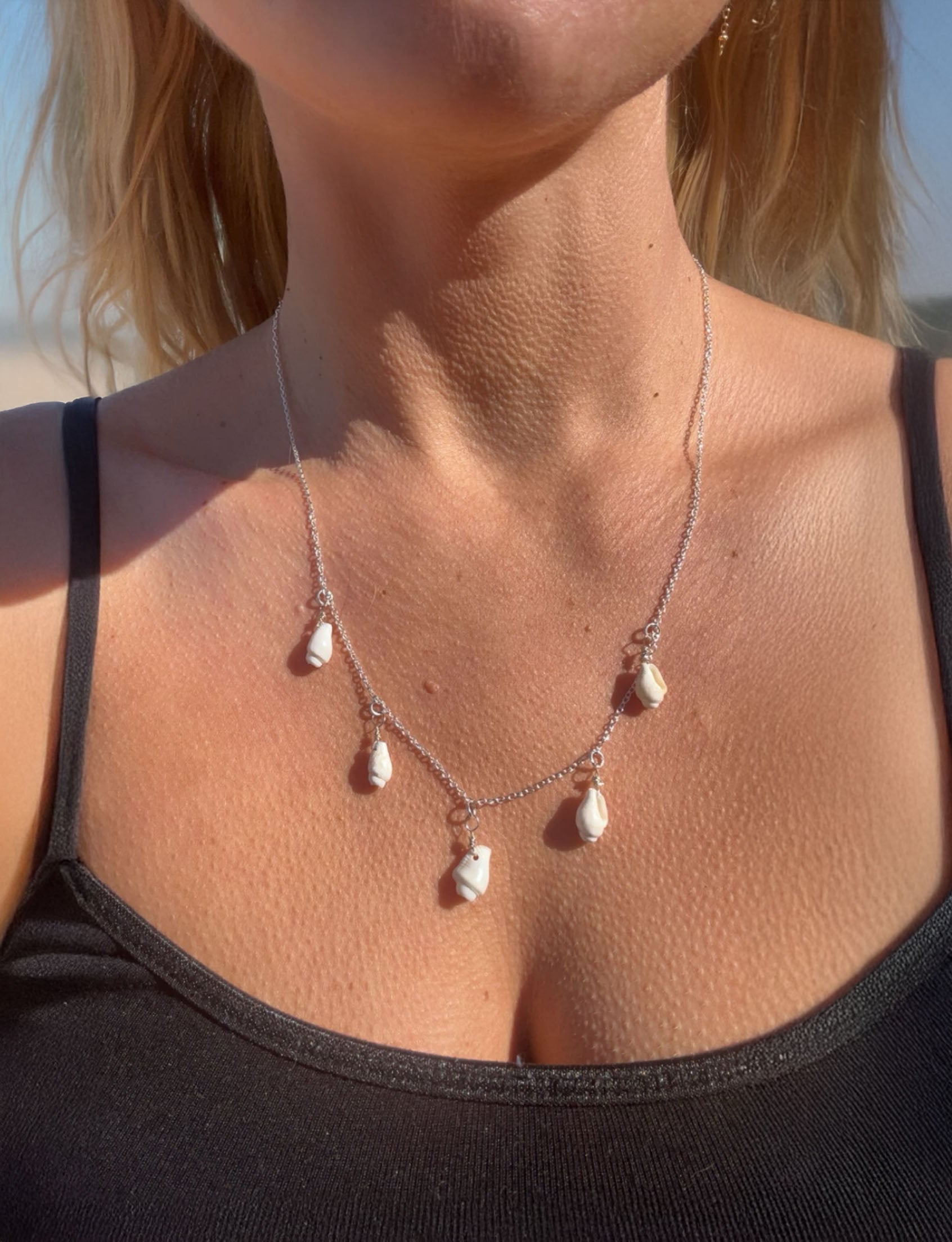 Necklace with tiny sheashells on a person wearing a black top against a blurred natural background.