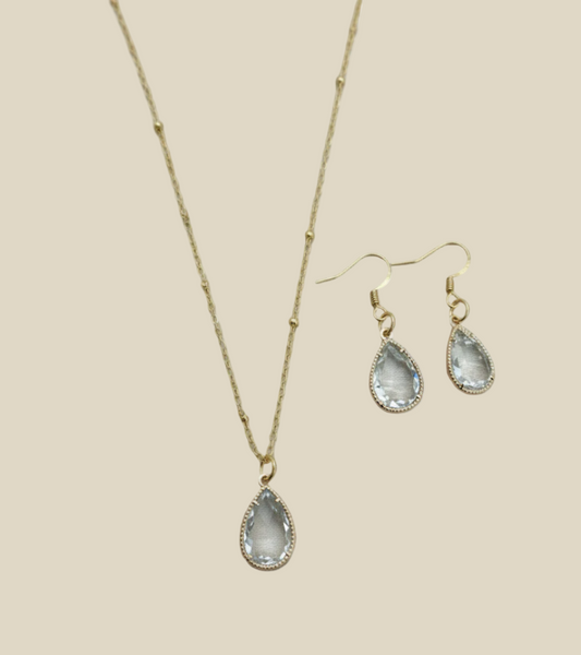 Teardrop-shaped jewellery set with necklace and earrings on a beige background.